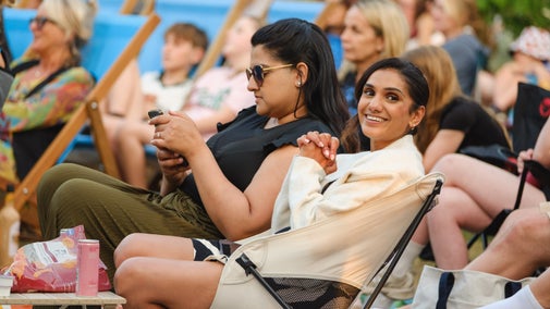An audience, including two young women, sitting in deckchairs and camping chairs to watch an outdoor movie